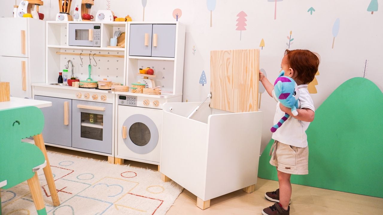 Criança brincando em ambiente montessoriano com cozinha infantil e baú organizador