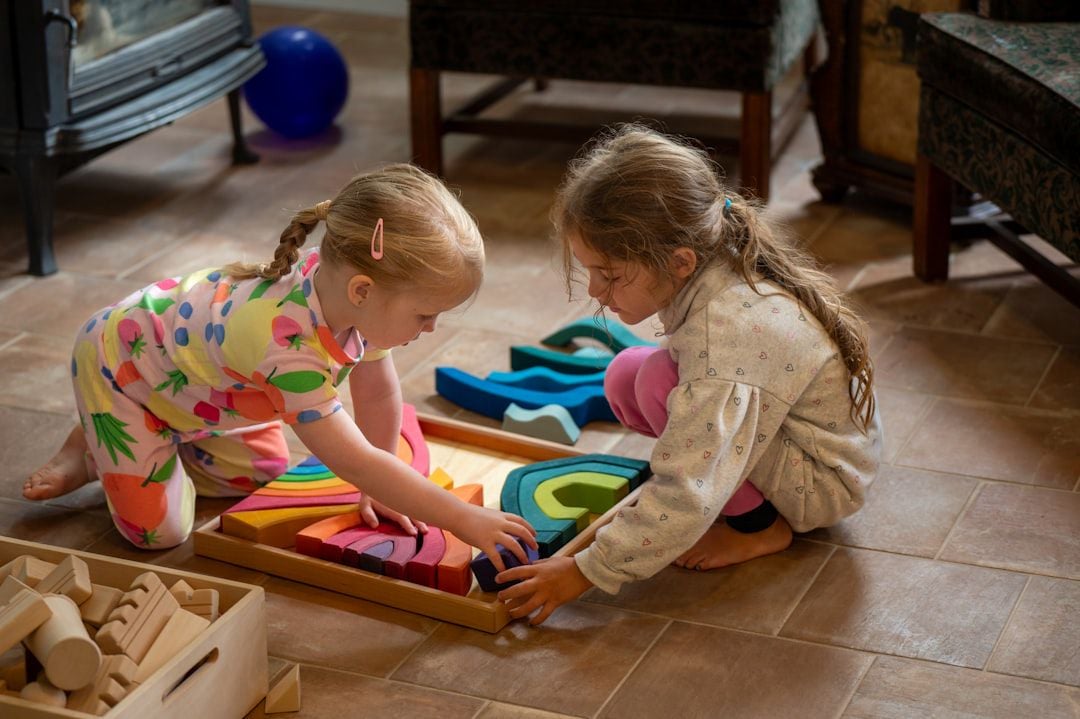 Duas meninas brincando com blocos de madeira coloridos dentro de casa — atividades para crianças em dias de chuva