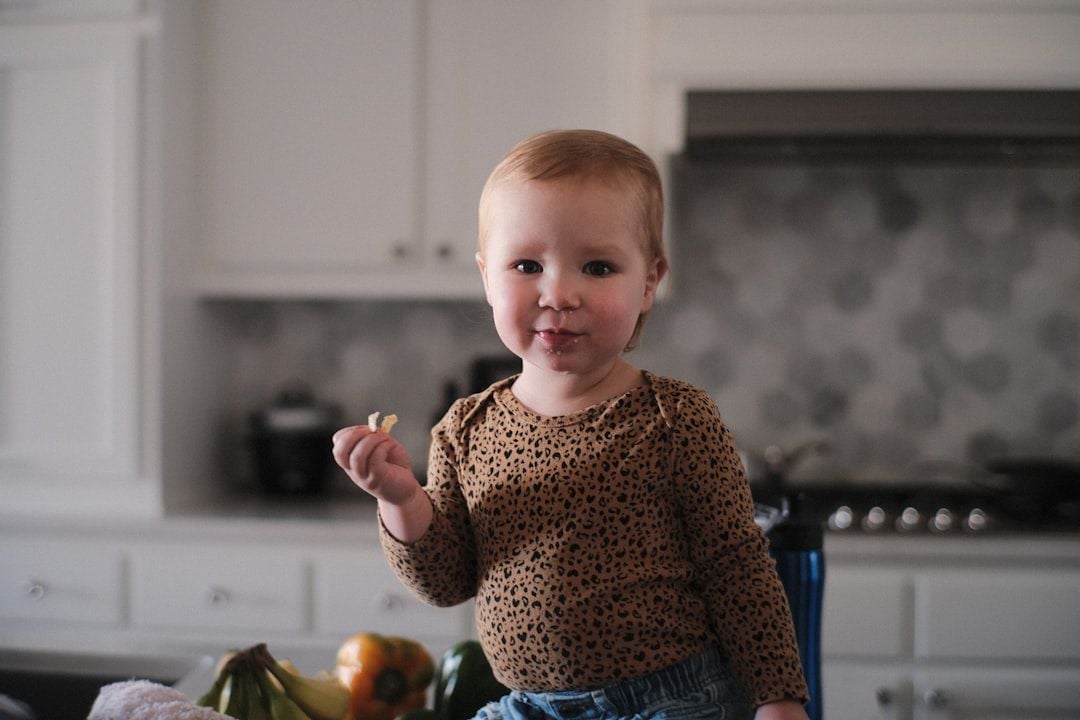 Menina pequena em cozinha segurando um alimento — cozinha infantil na introdução alimentar