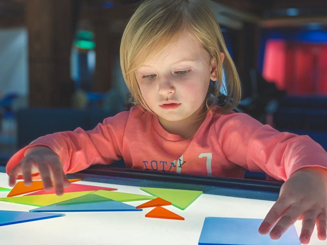 Criança segurando formas coloridas translúcidas — atividade sensorial com mesa luminosa Montessori
