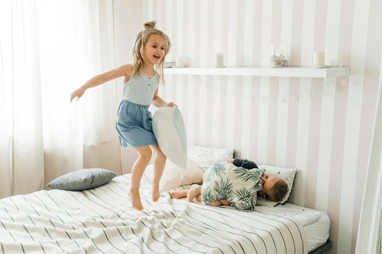 Duas crianças brincando e pulando na cama em quarto compartilhado entre irmãos