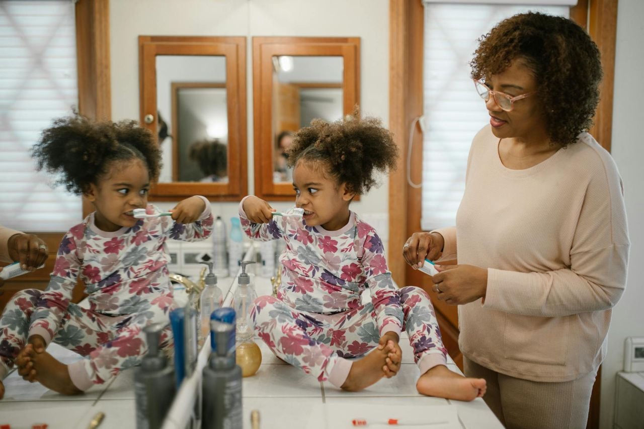 Menina em pijama escovando os dentes com a mãe — rotina visual Montessori para crianças de 2 a 6 anos